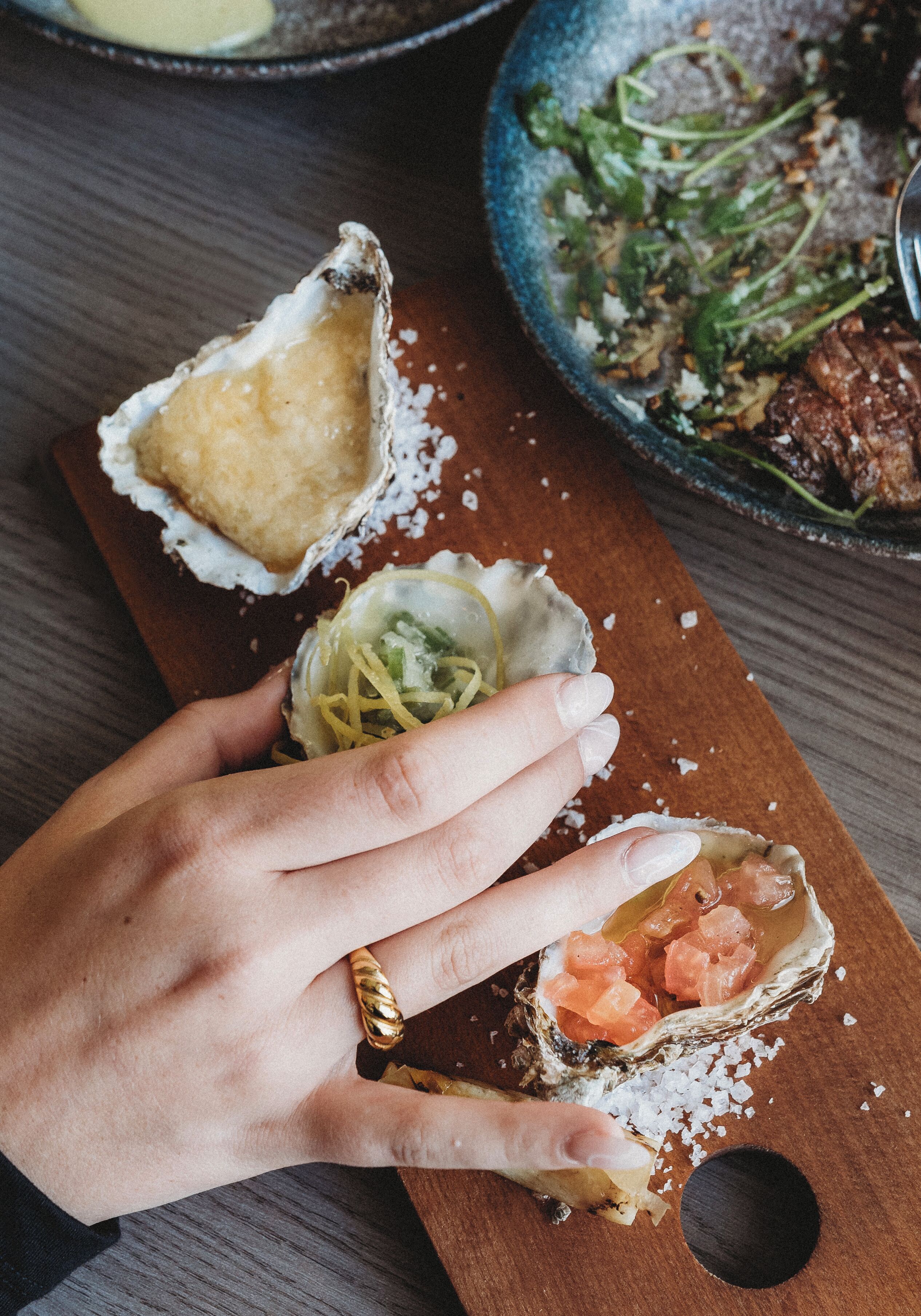 A hand holding a piece of food with a wooden board and a bowl in the background.