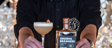 A person in a black shirt at a bar with a bottle of Smugglers Branneri and a martini glass.