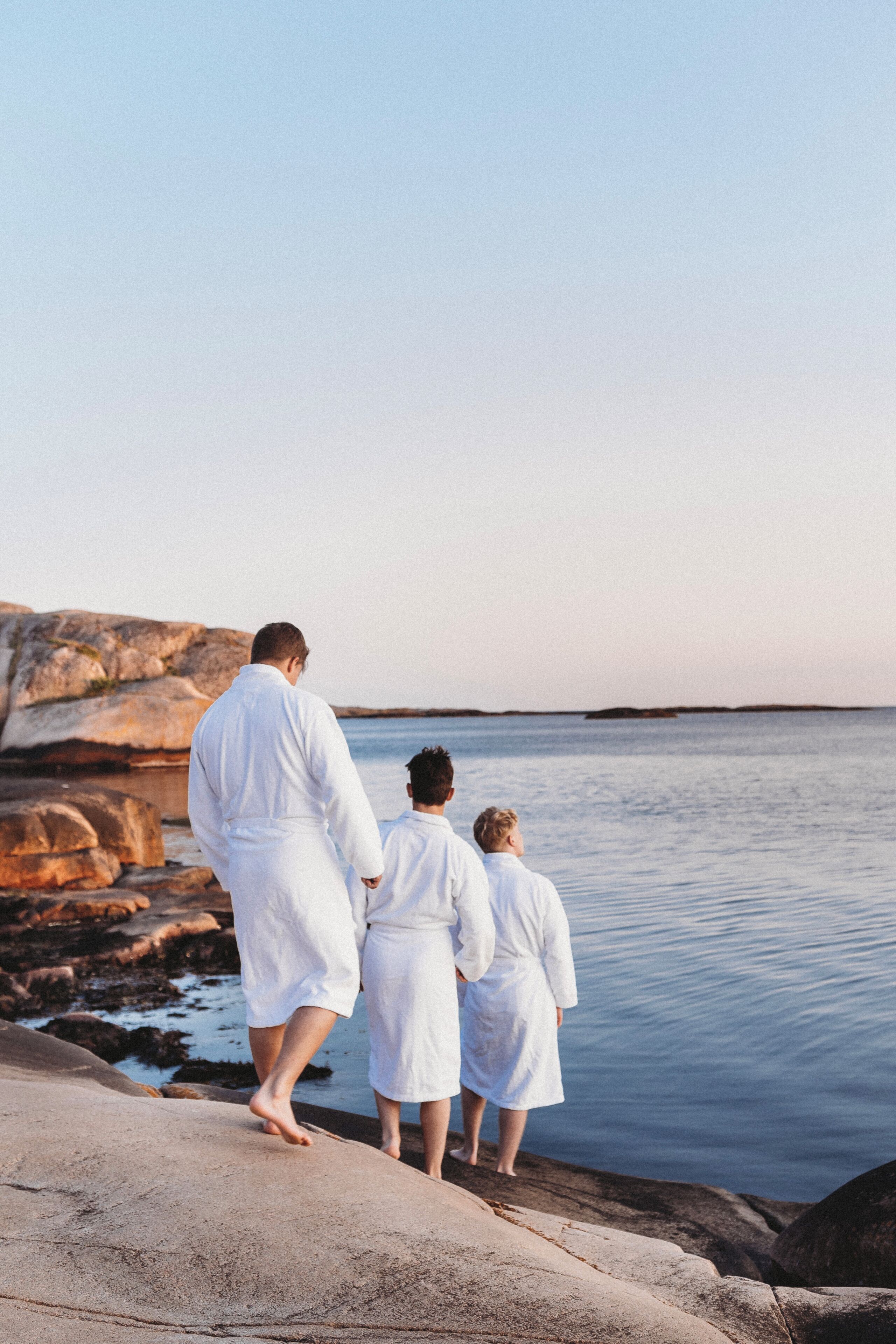 Tre personer i vita dräkter som står på en stenstrand vid havet.