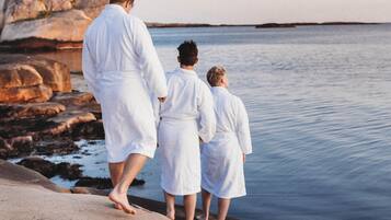 Tre personer i vita dräkter som står på en stenstrand vid havet.