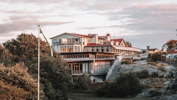 A multi-story building with a prominent flag, surrounded by trees and rocky terrain.