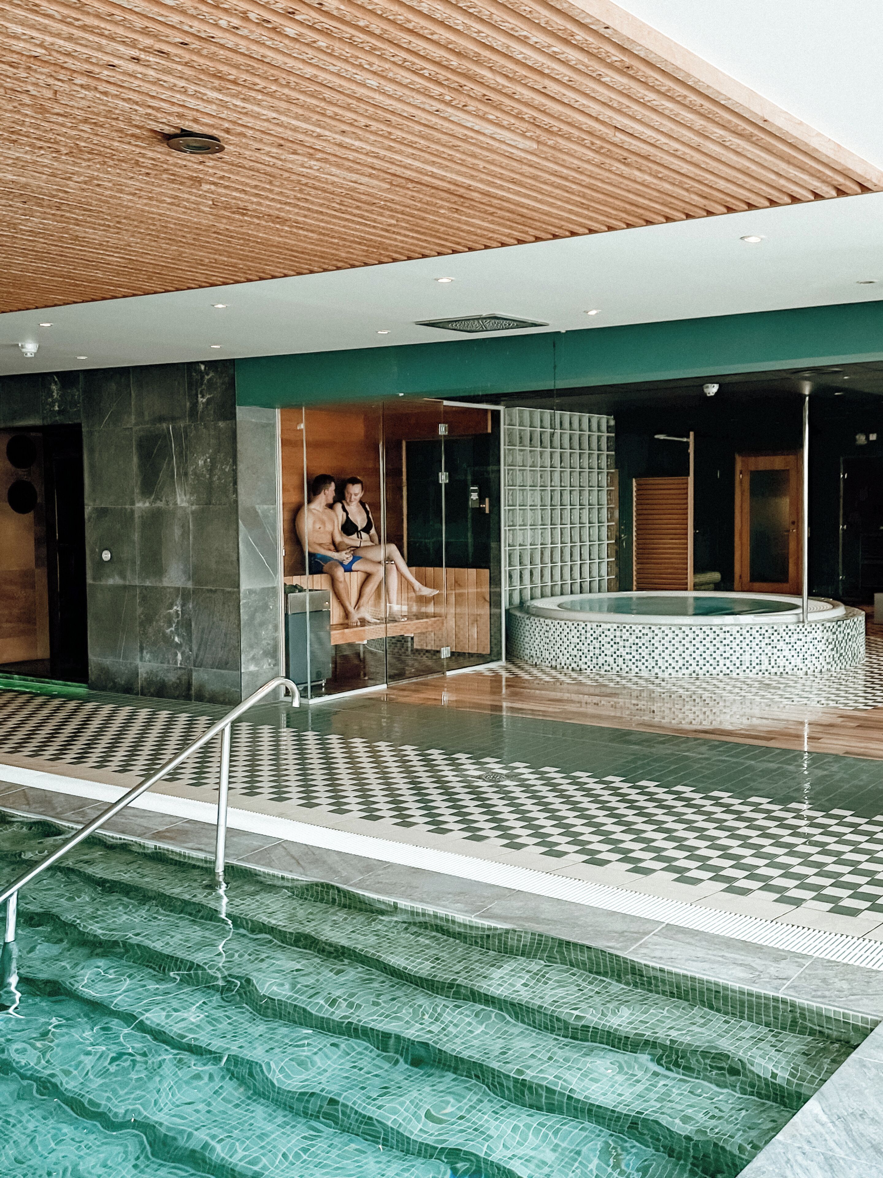Area piscina interna moderna con pavimento a scacchi, zona relax con un grande murale e vasca idromassaggio.