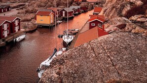 A coastal village with traditional red-roofed houses, a rocky shoreline, and boats docked in the water. - Smögens Hafvsbad (Smogen)