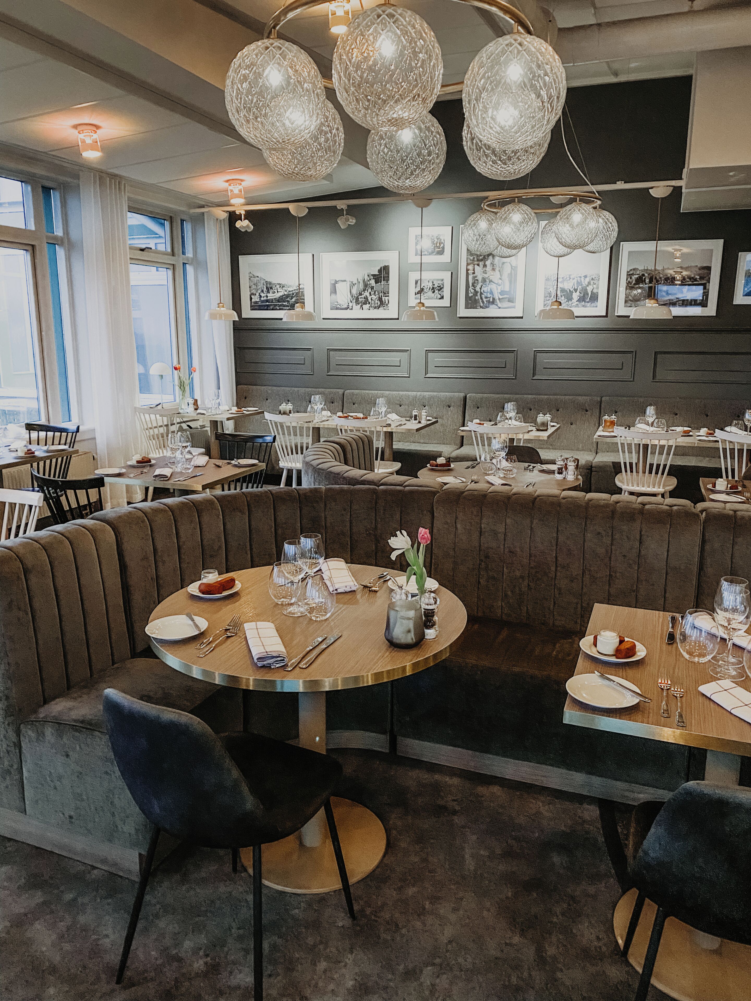 A restaurant with round tables, cushioned booths, and pendant lighting.