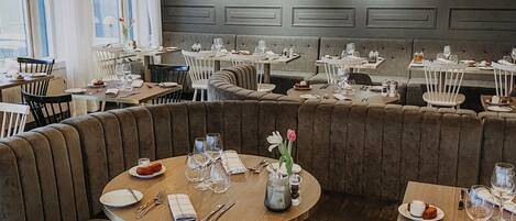 A restaurant with round tables, cushioned booths, and pendant lighting.