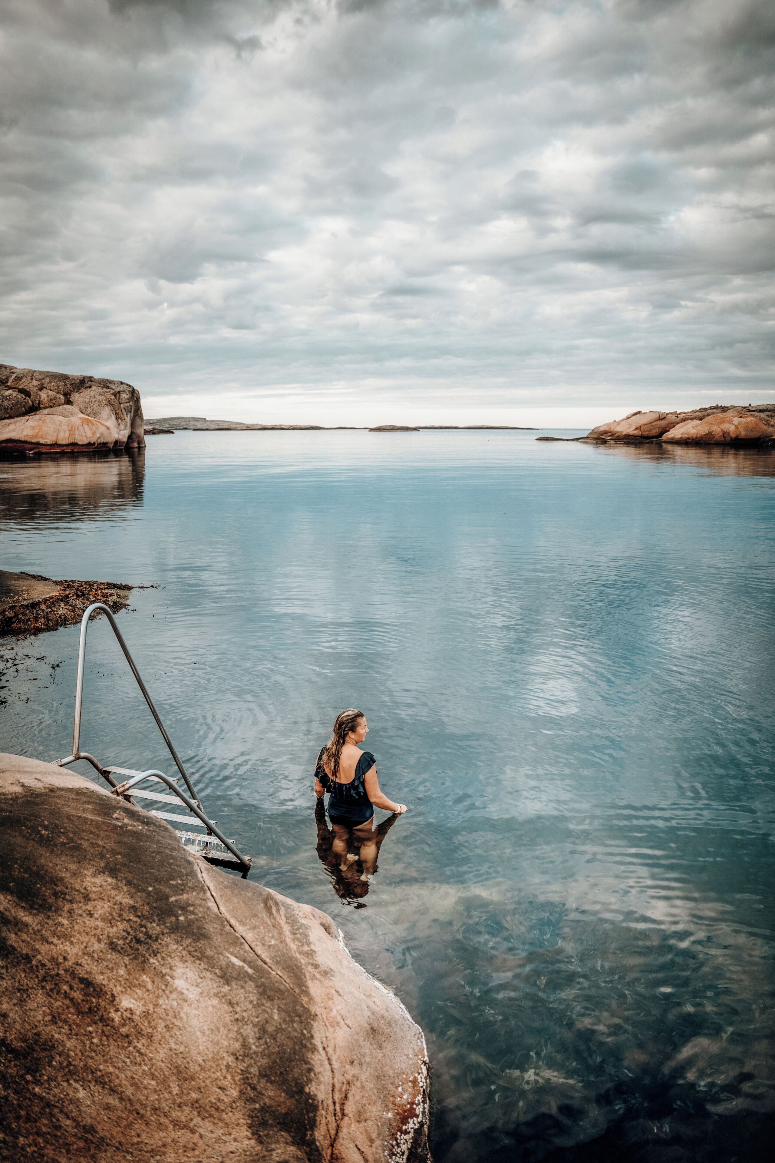 A woman standing at the edge of a clear pool with rocky formations in the background.
