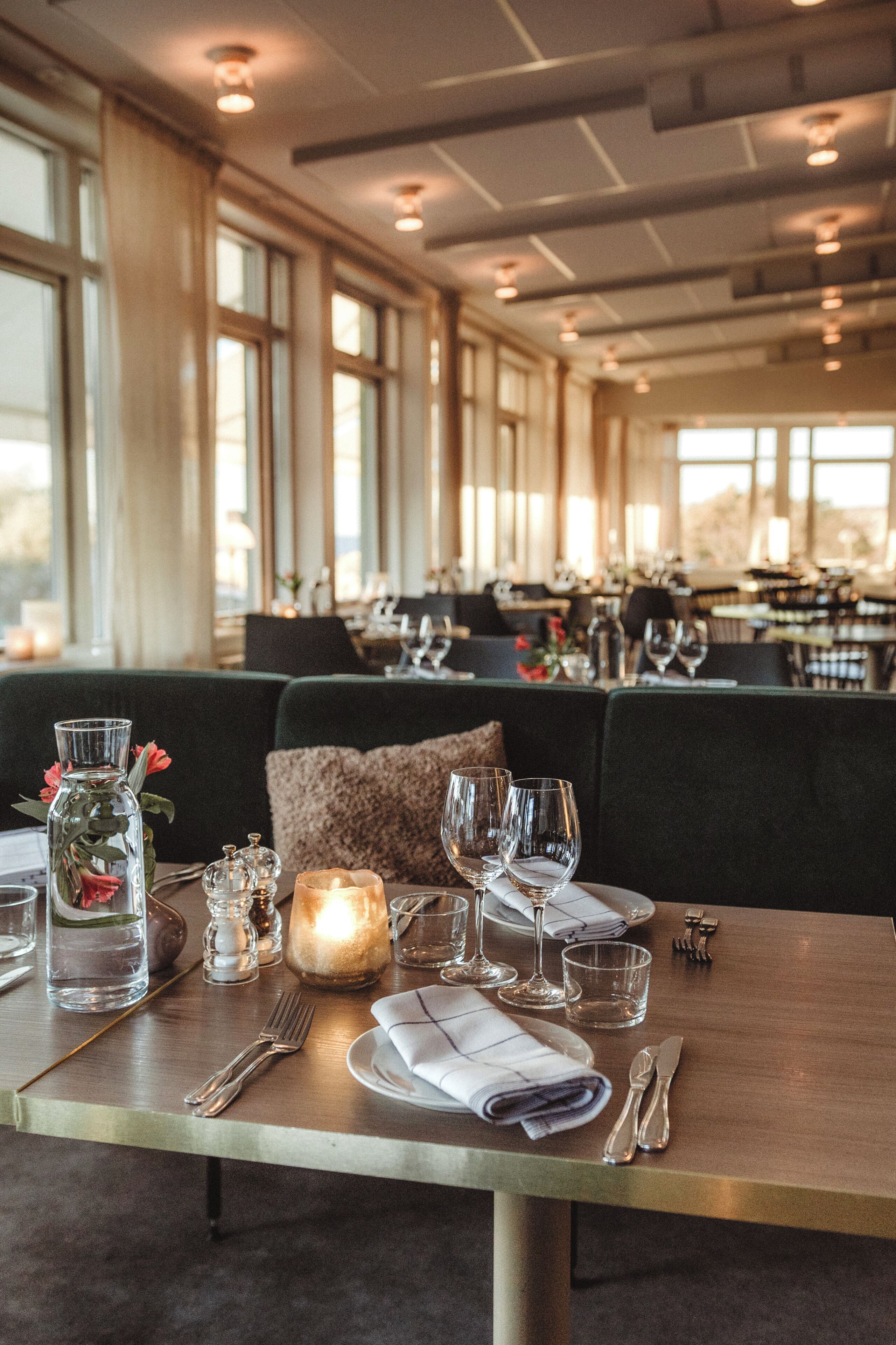A dining table set with a candle, glasses, and cutlery in a restaurant with large windows and a modern interior.