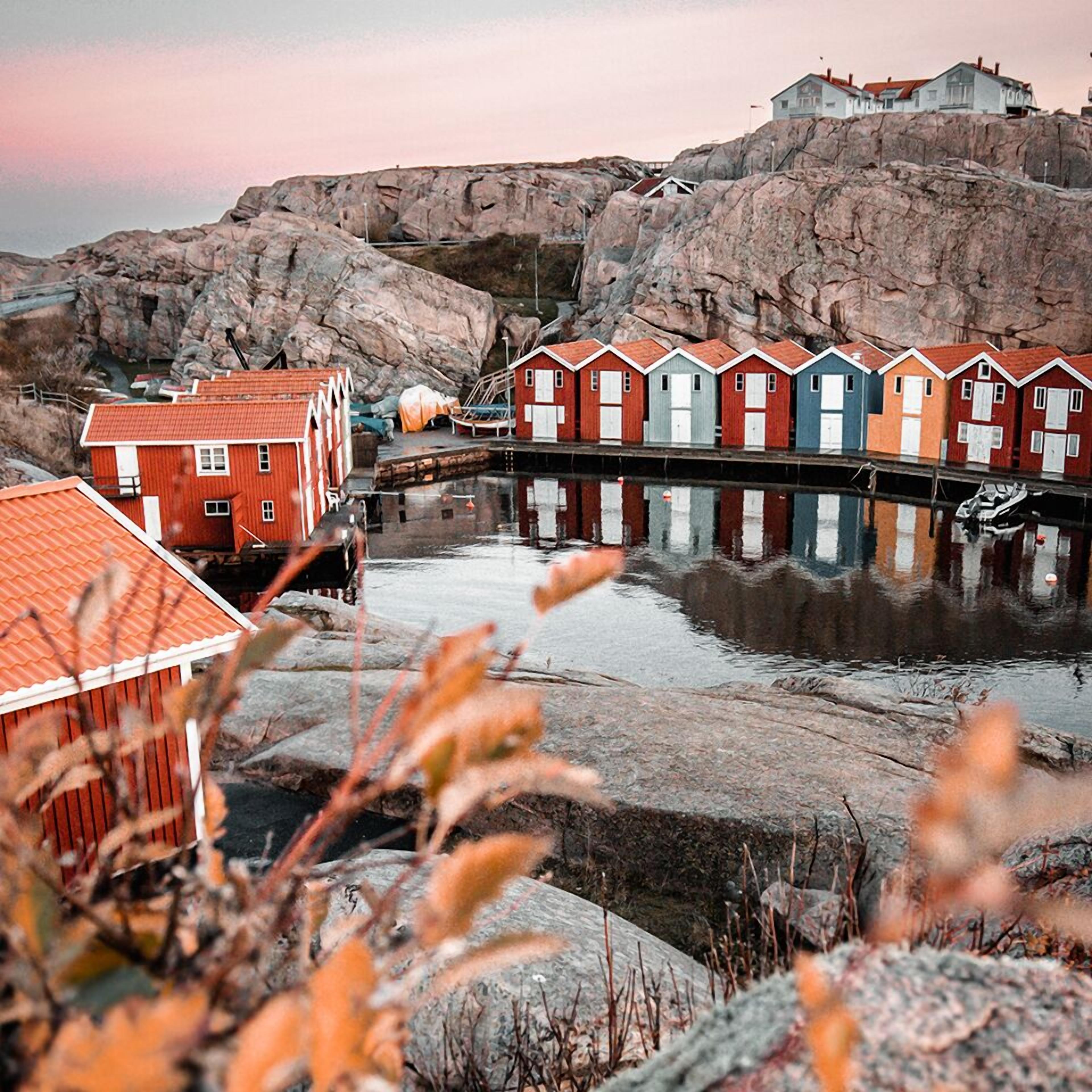 A waterfront property with a row of colorful wooden houses, a rocky backdrop, and a calm body of water.