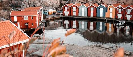 A waterfront property with a row of colorful wooden houses, a rocky backdrop, and a calm body of water.