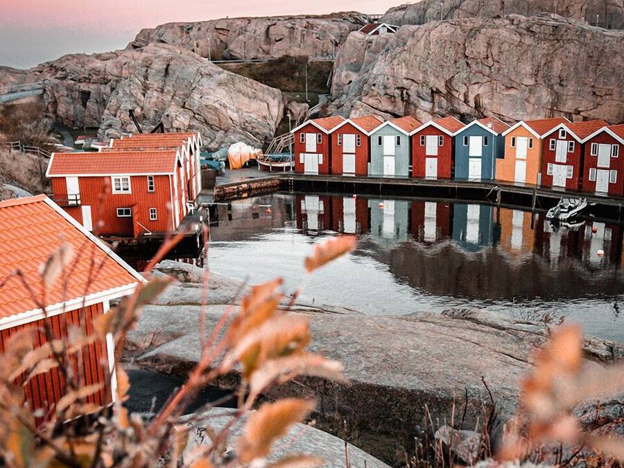 A waterfront property with a row of colorful wooden houses, a rocky backdrop, and a calm body of water.
