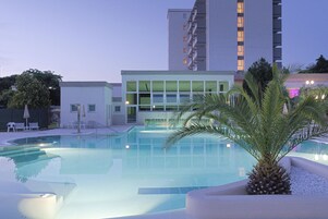 Una piscina con un edificio moderno al fondo, una palmera y sillas de descanso.