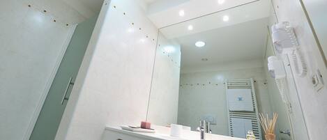 A modern bathroom with a large mirror, white countertop, and a towel rack.