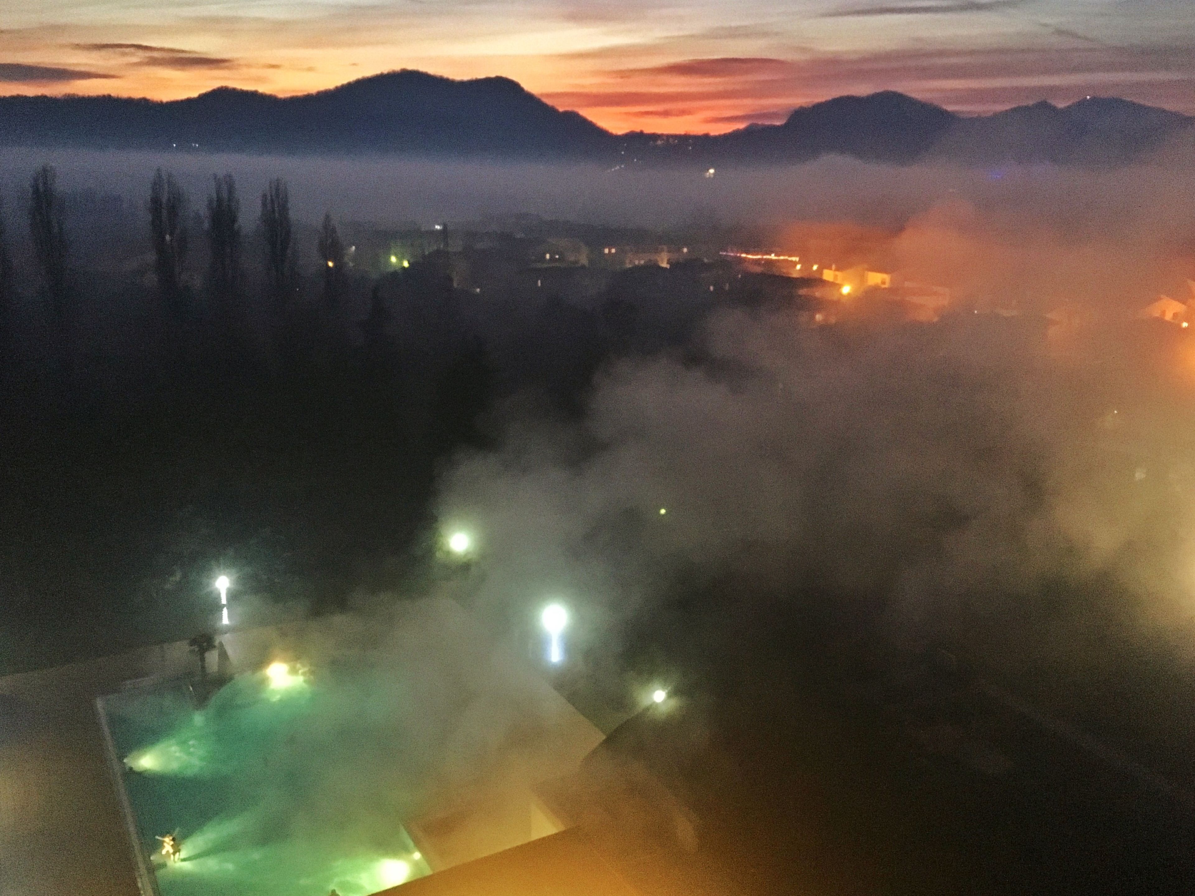 Nachtsicht auf eine Berglandschaft mit dichter Nebelstimmung und entfernten Stadtlichtern.