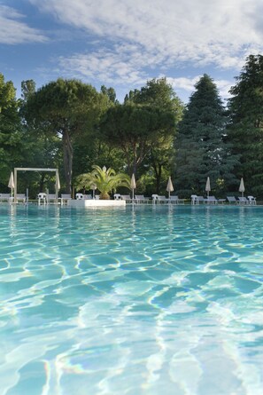 Una piscina cristalina con sillas de descanso y sombrillas, rodeada de árboles.