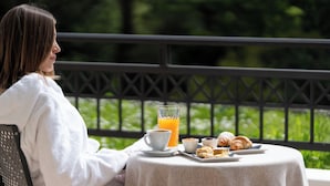 A person seated at a table with a breakfast setting including croissants, a cup of coffee, and a glass of orange juice.