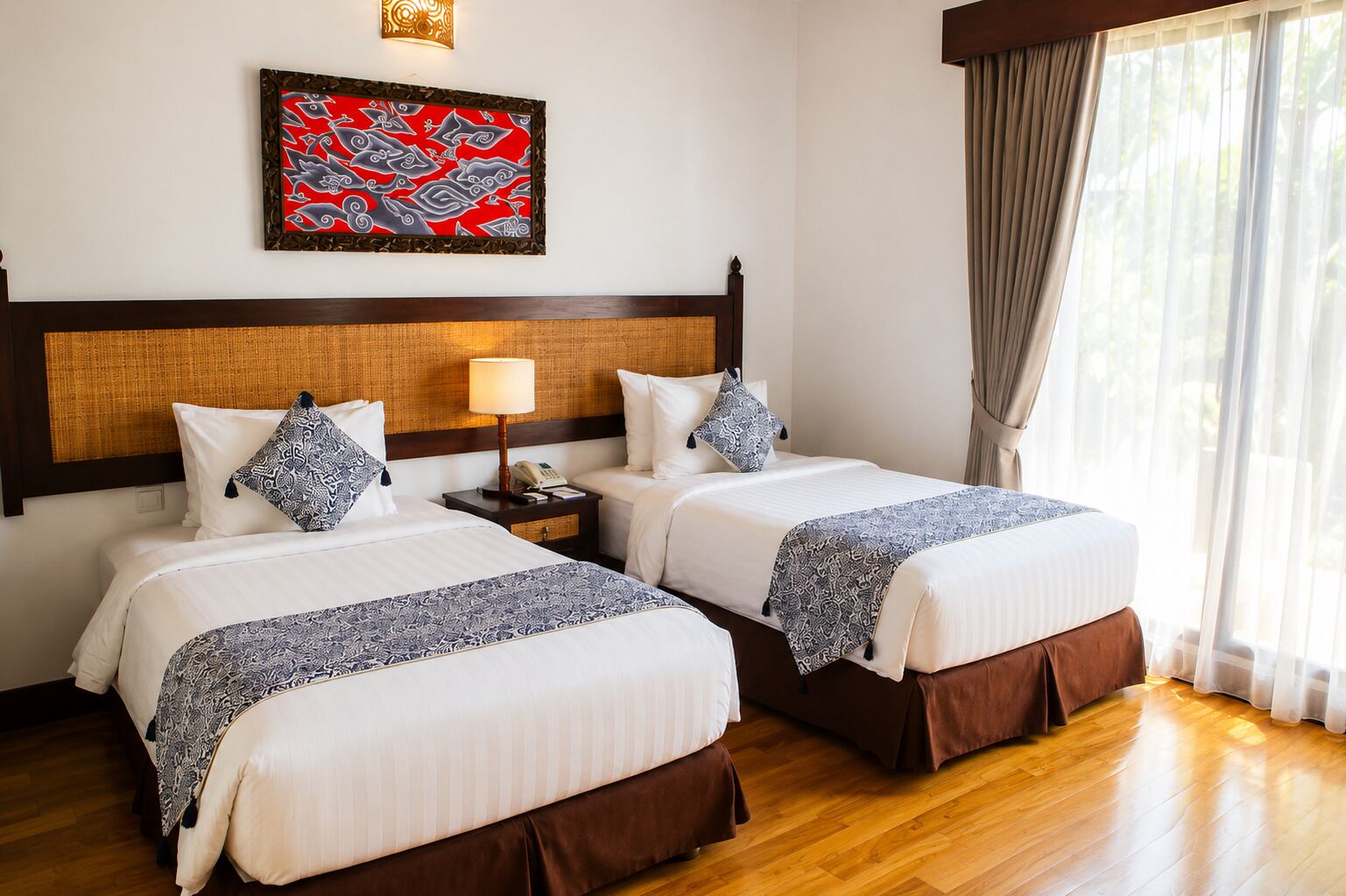 Ein Hotelzimmer mit zwei Betten, einem Holz-Kopfteil, einem an der Wand befestigten Kunstwerk, einem Nachttisch mit Lampe und einem Fenster mit Vorhängen.