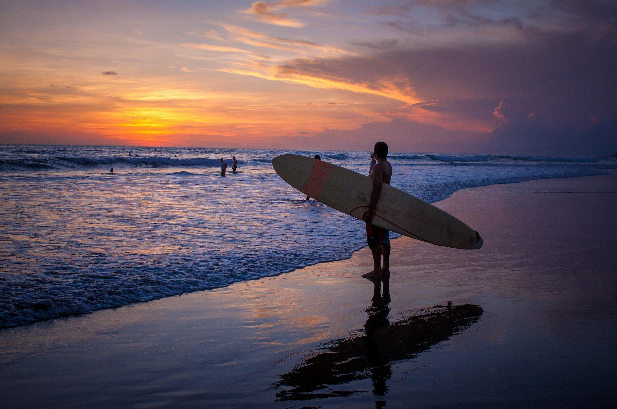 A beach scene with a person holding a surfboard, waves, and a sunset.