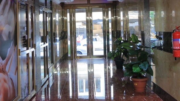 A hotel lobby with a polished marble floor, a reception desk, a fire extinguisher, and a large potted plant.