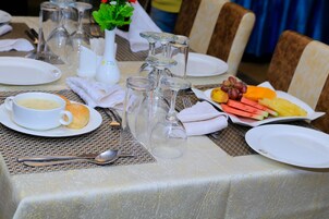 Una mesa de comedor dispuesta con platos, vasos y cubiertos, junto con un tazón de sopa y un plato de fruta.