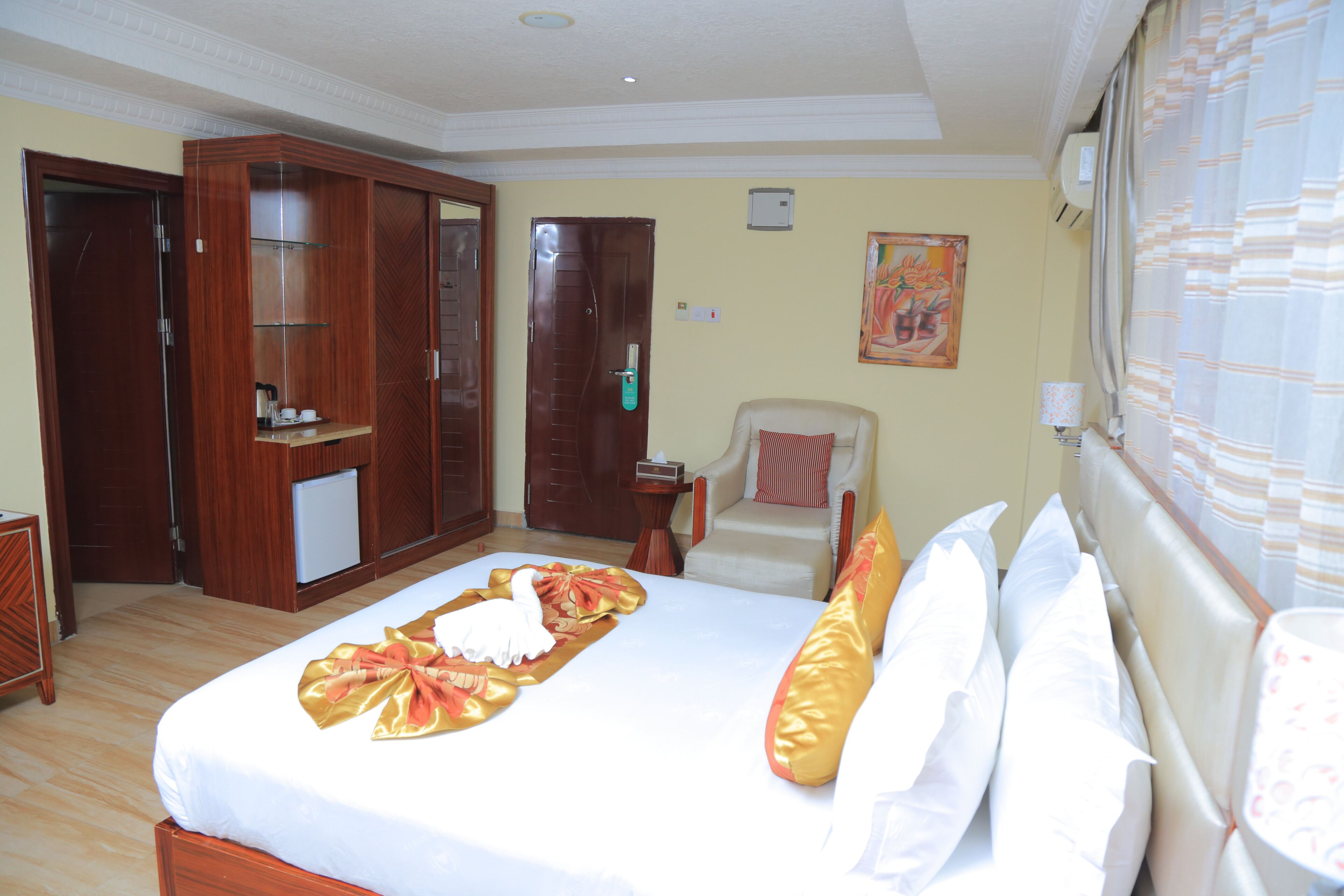 A hotel room with a large bed, a wardrobe, a chair, and a painting on the wall.
