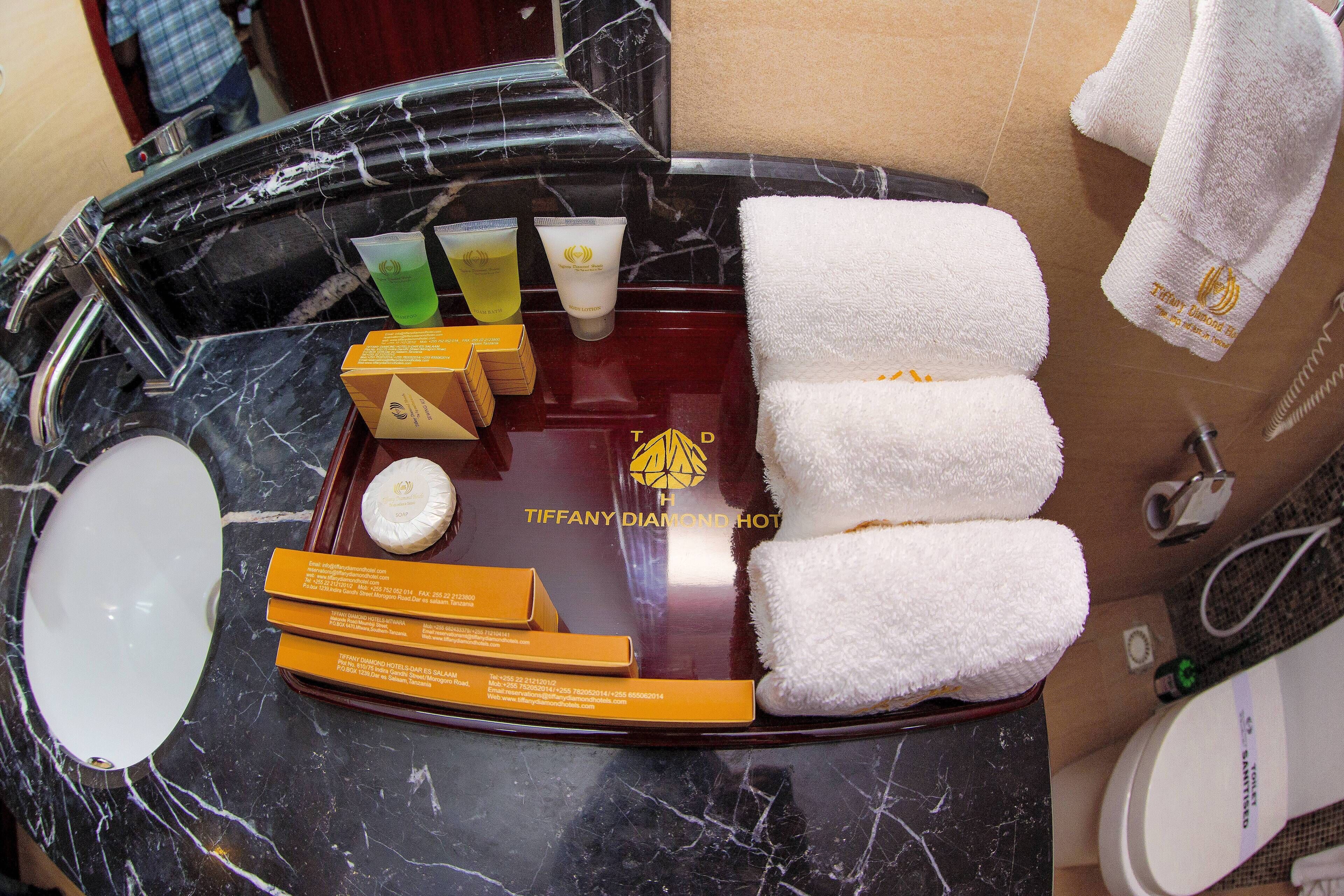 Un mobile bagno con piano in marmo, un lavandino bianco e uno specchio. Sono presenti tre asciugamani bianchi, una bottiglia di shampoo e una confezione di articoli da toilette.