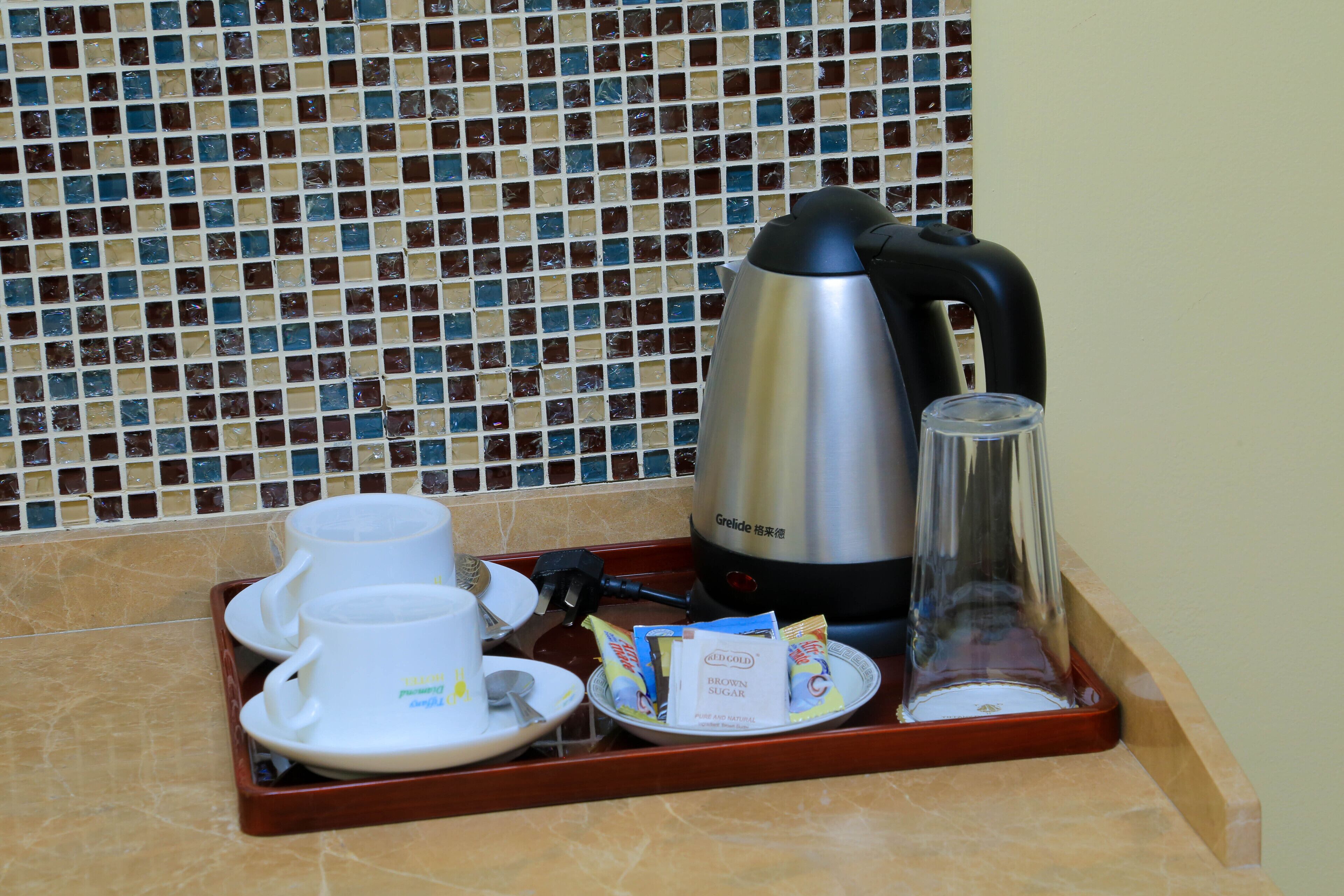 A tray with a coffee maker, cups, and sugar packets on a tiled countertop.