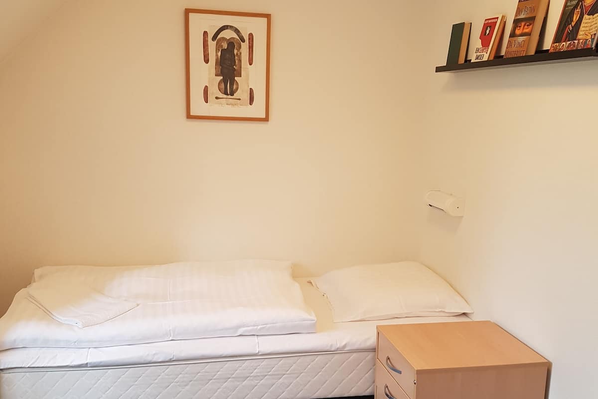 A small, single-bed room with a mattress, a wooden box, and a framed picture on the wall.