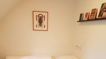 A small, single-bed room with a mattress, a wooden box, and a framed picture on the wall.