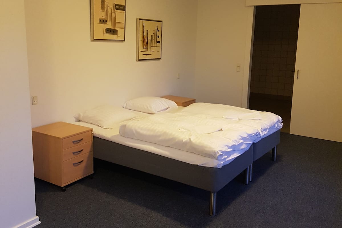 A bedroom with a bed, a nightstand, a dresser, and two framed pictures on the wall.