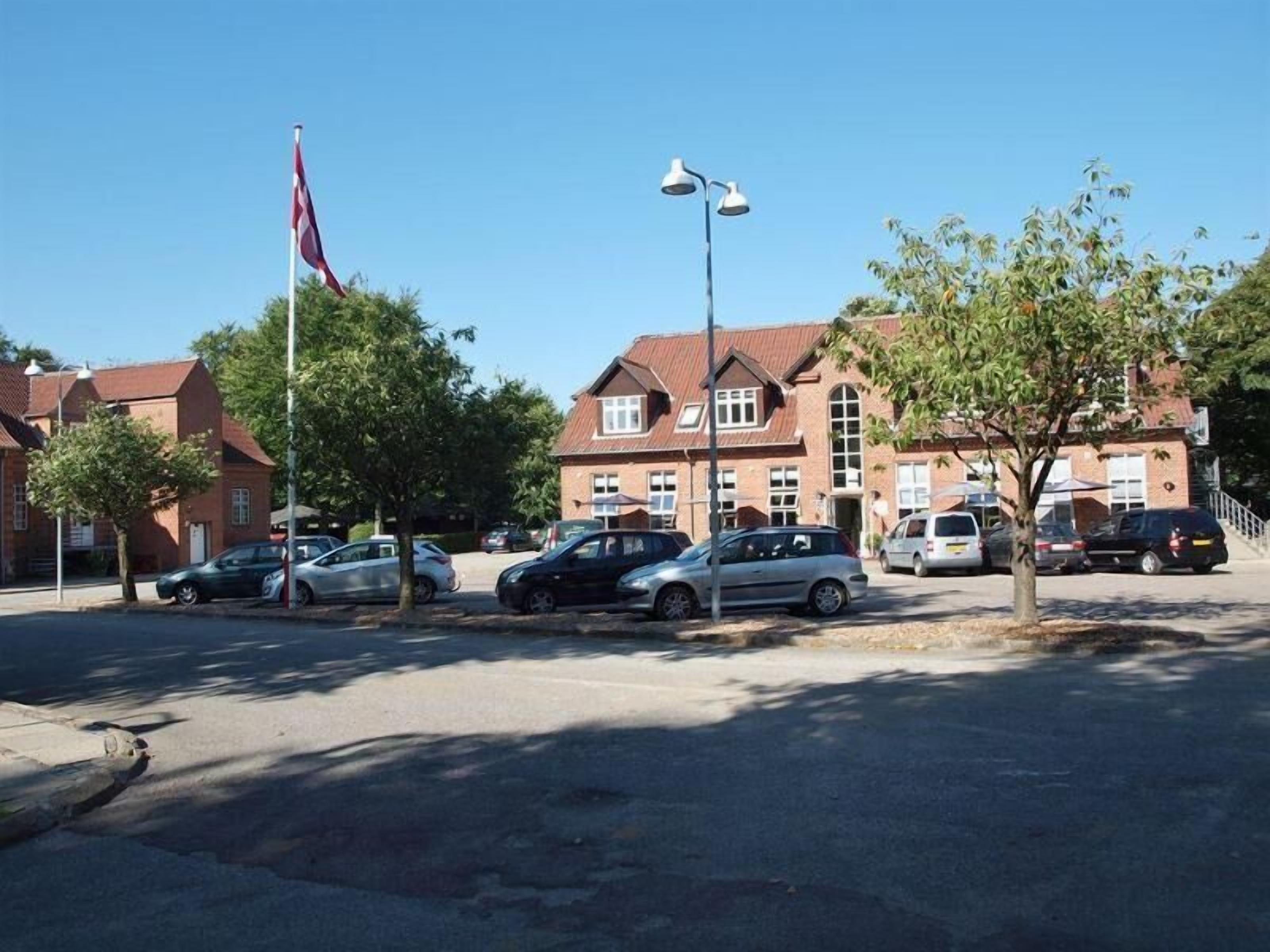 A parking lot with several cars, a flag, and a building with a red roof.