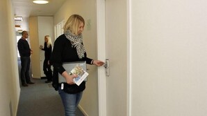 A person in a hallway holding a magazine, with a door to the right and other individuals in the background. - Danhostel Brande (Brande)
