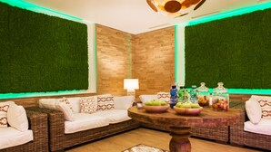 Een gezellig zithoekje met rieten banken, een ronde houten tafel met fruit en potjes, en een groene wand.