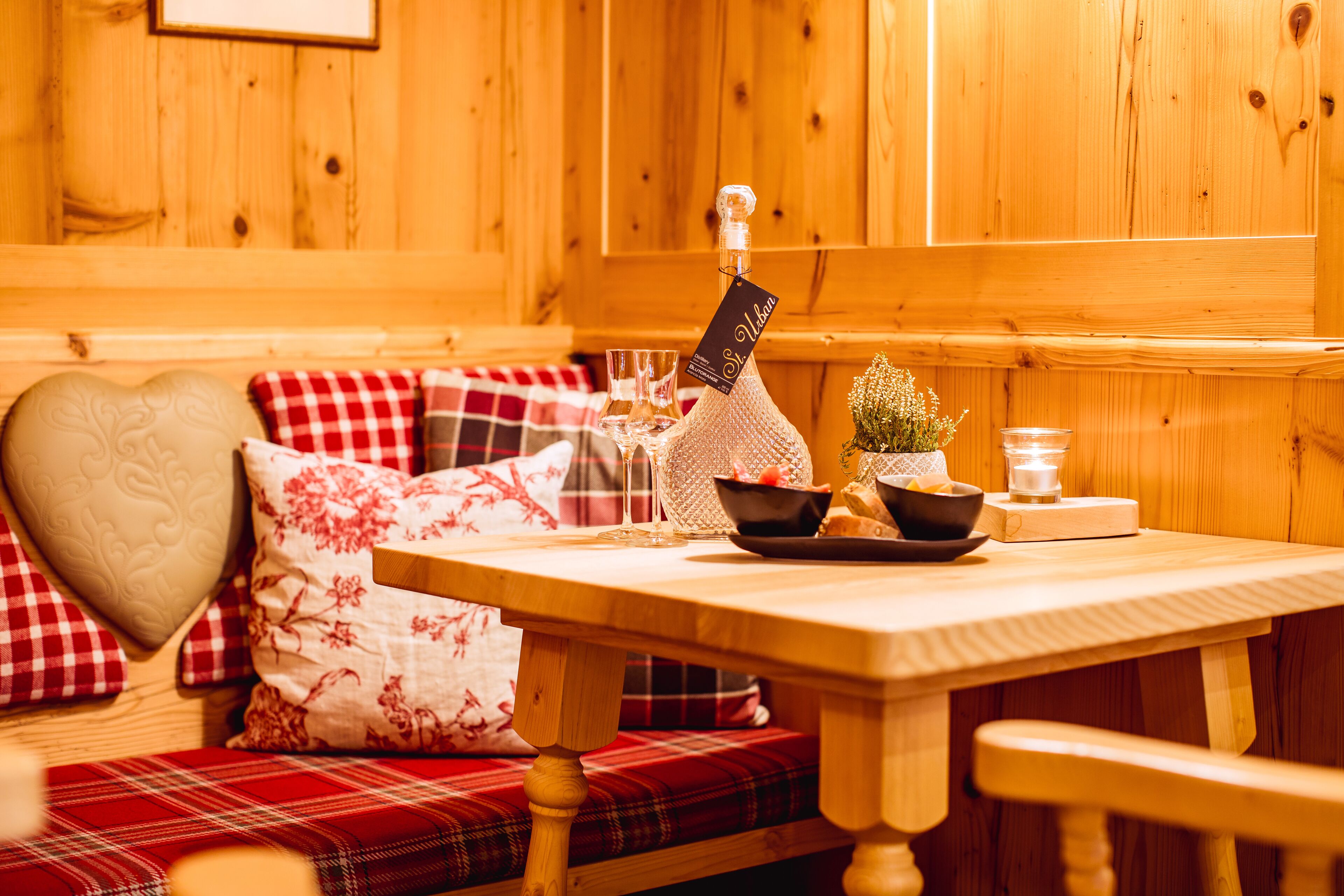Een houten interieur met een bank, een tafel met een fles, glazen en een schaal.