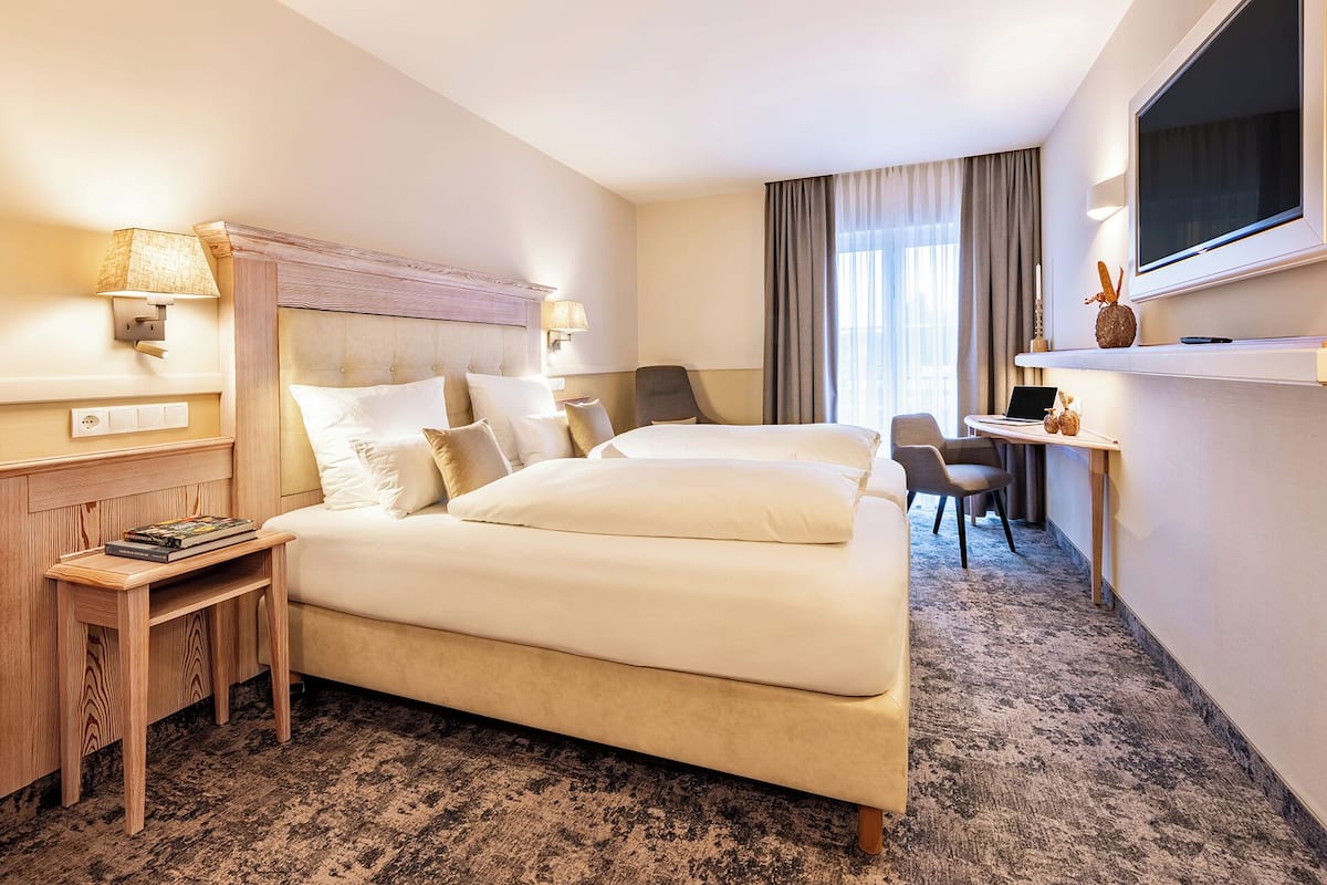 Ein Hotelzimmer mit einem großen Bett, einem Schreibtisch mit einem Laptop, einem Fernseher und einem kleinen Tisch mit Büchern.