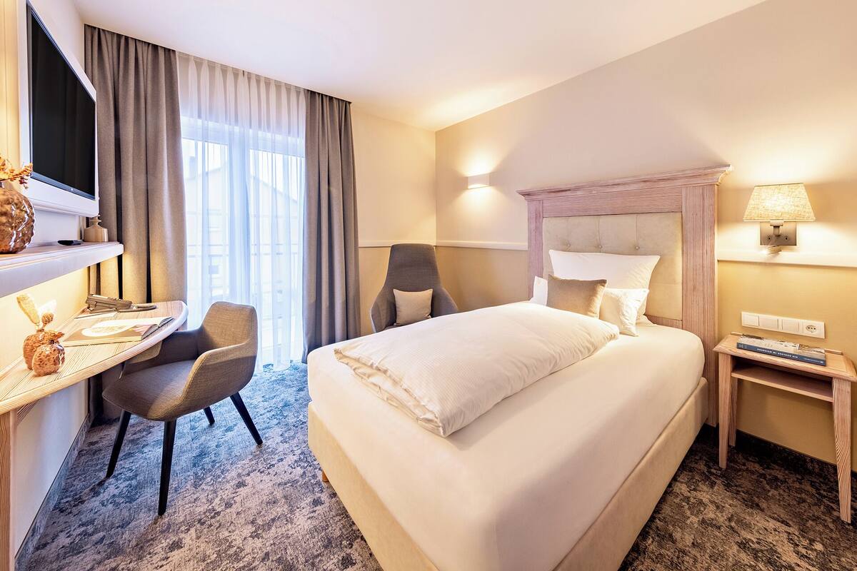 Ein Hotelzimmer mit einem großen Bett, einem Schreibtisch mit Stuhl, einem Fernseher und einer Lampe.