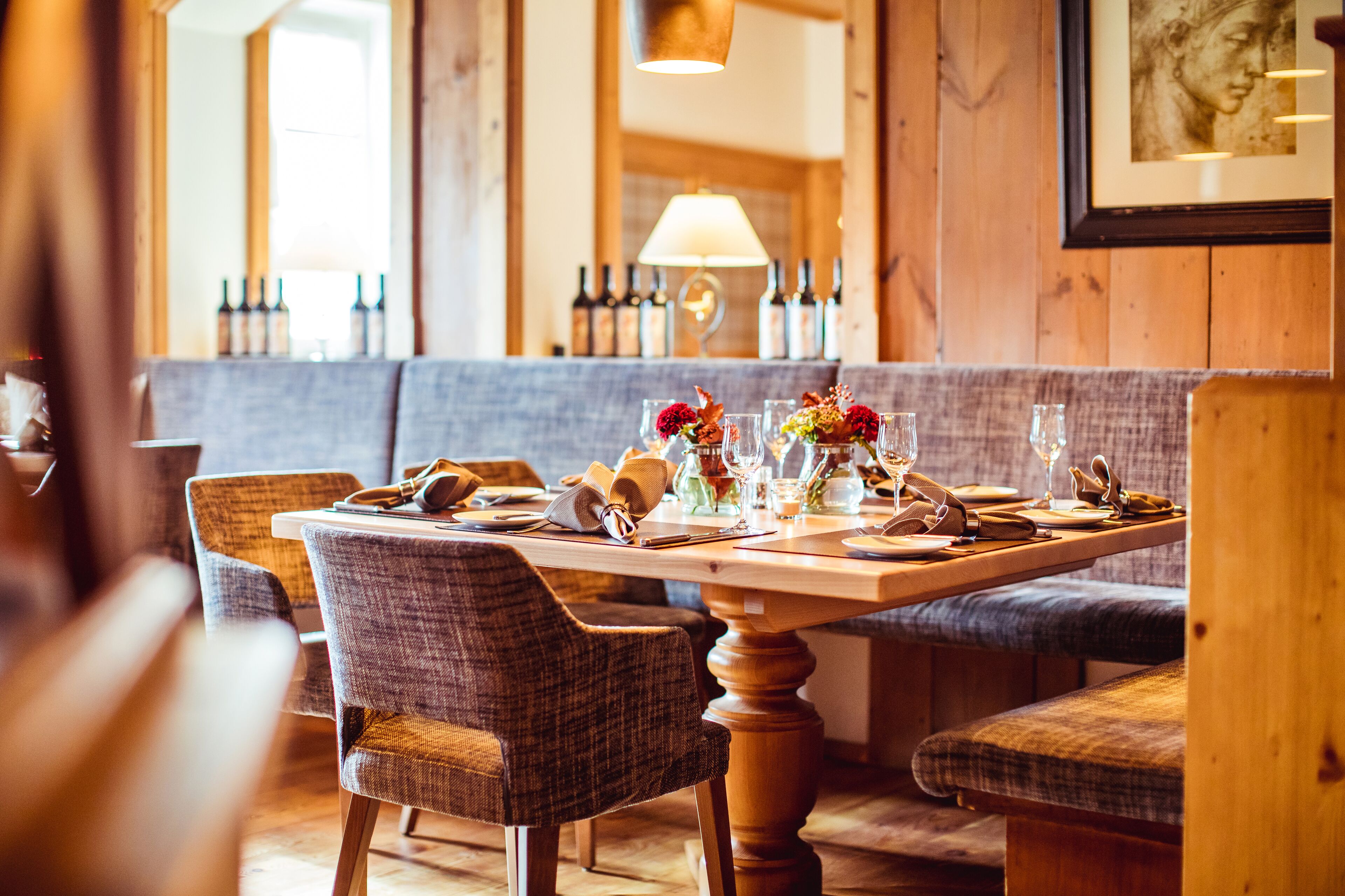 A restaurant interior with a wooden table set for dining, upholstered chairs, and a bench.