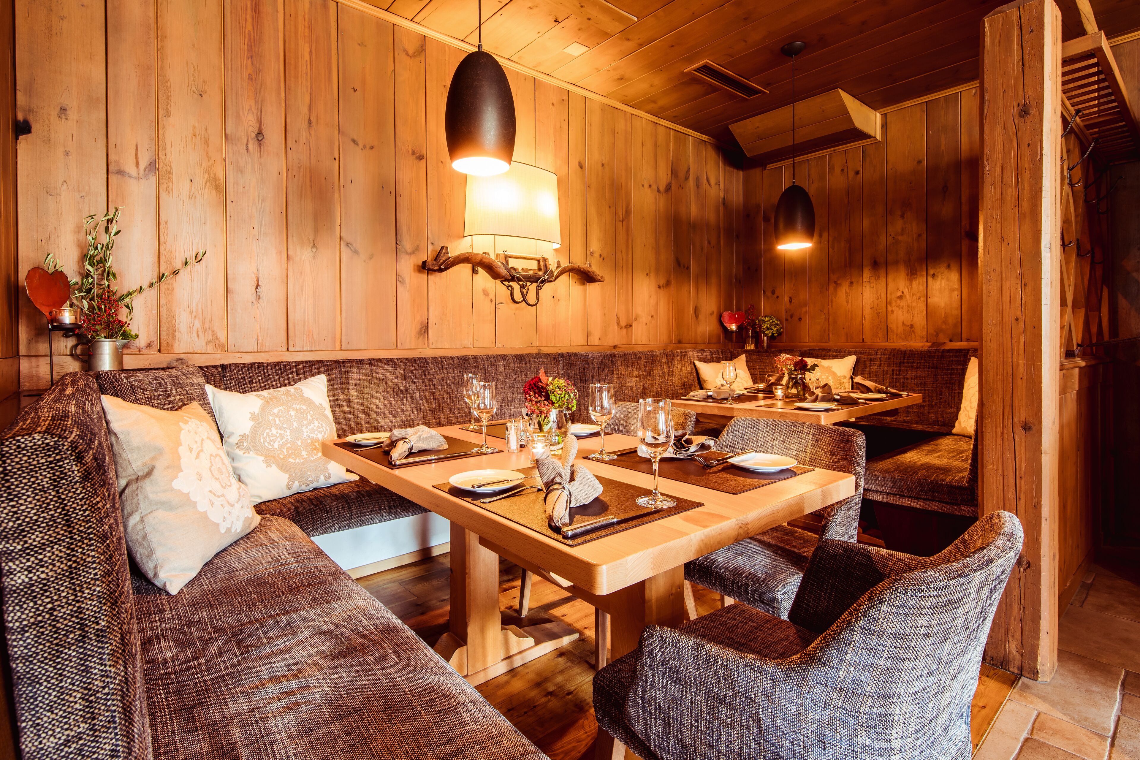 A wooden interior with a dining table set for two, surrounded by upholstered sofas and chairs.