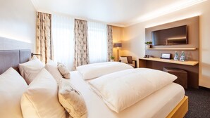 Hotelkamer met een groot bed, een bureau met een flatscreen televisie, een stoel en een tafeltje met een plant en flessen.