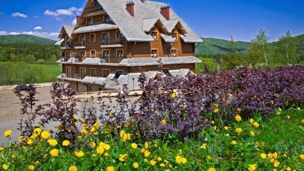 A multi-story wooden chalet with a sloped roof, multiple balconies, and a scenic mountain backdrop.