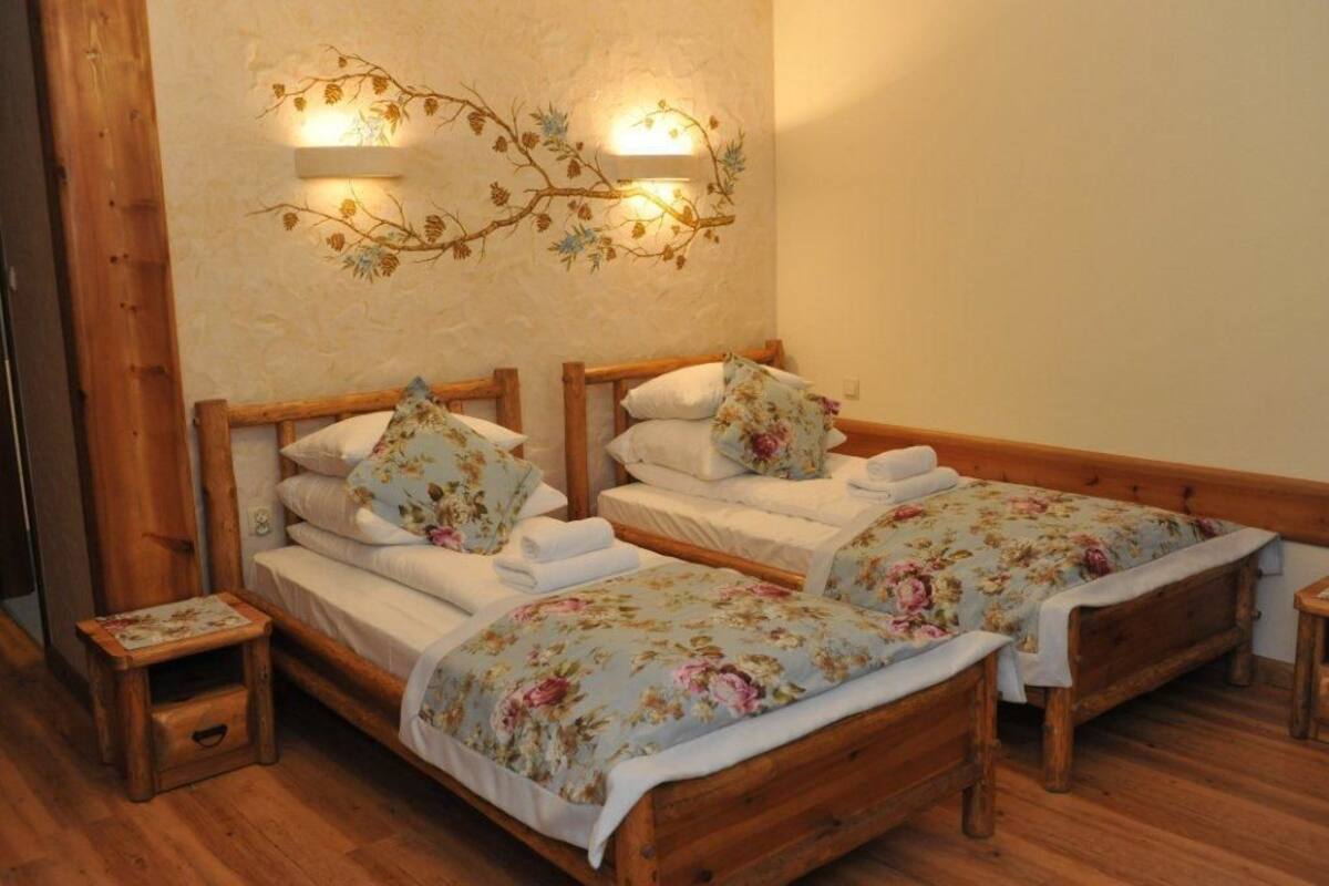 Une pièce avec deux lits en bois, chacun agrémenté de draps et d’oreillers à motifs floraux. On y trouve également des lampes fixées au mur et un petit tabouret en bois.