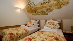 A room with two beds, each with floral bedding and matching pillows. There is a wall-mounted light fixture and a mural depicting a natural scene with animals.