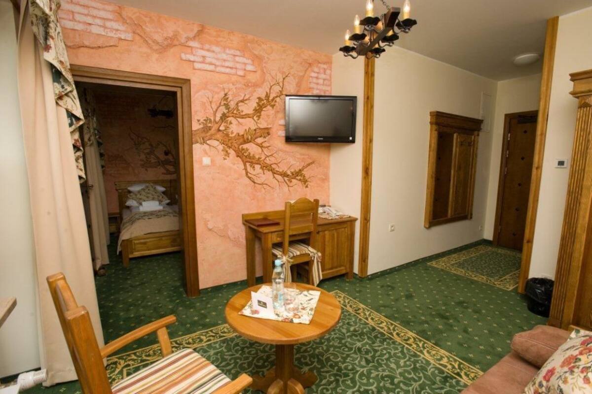 Une pièce comprenant un lit, une table en bois avec une chaise, un téléviseur fixé au mur et un tapis à motifs.