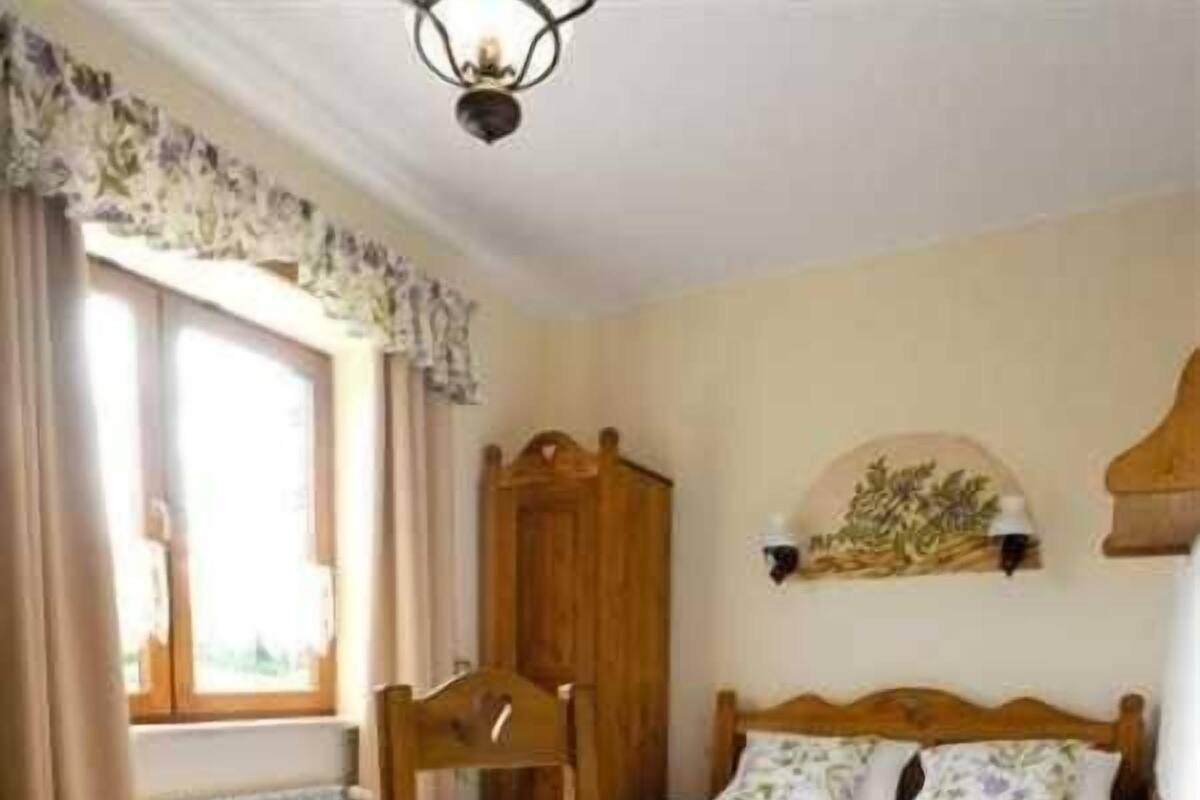 Une chambre avec deux lits, une armoire en bois, une chaise, une table et une fenêtre avec des rideaux.