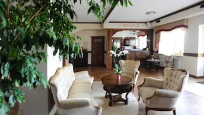 A spacious lobby with a reception desk, a dining area, and a seating area with a round table and four armchairs.