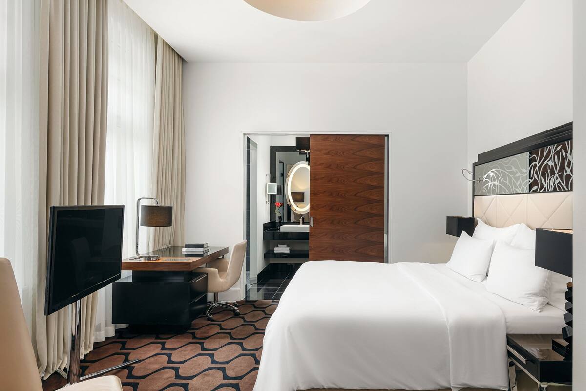 Habitación de hotel con cama, escritorio, televisor y baño visible a través de una puerta abierta.