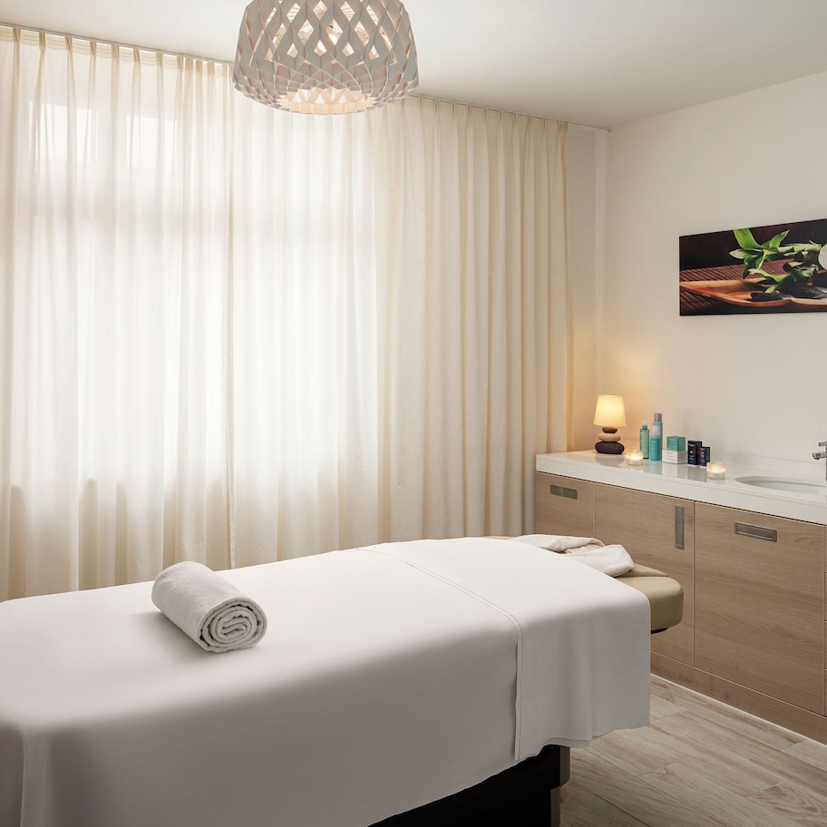 A modern spa room with a massage table, a sink, and a mirror.