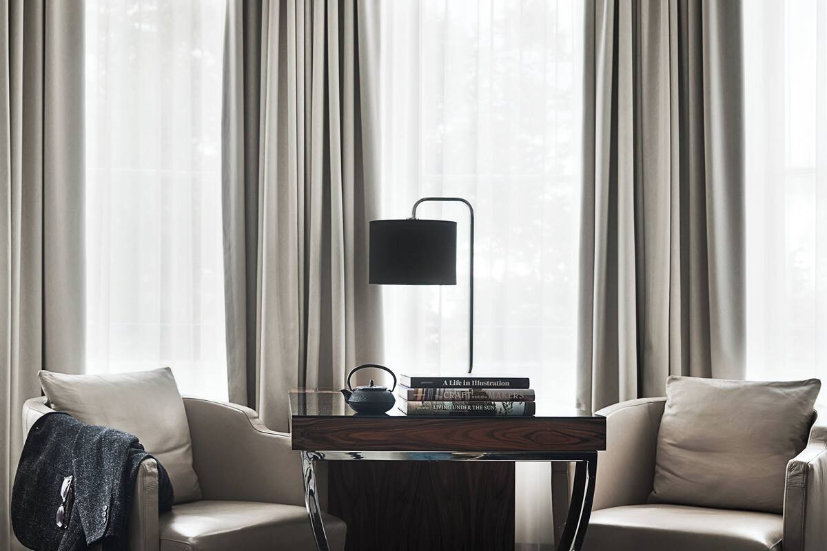 Una sala de estar moderna con un sofá, una mesa de centro y una lámpara. Se ven cortinas y una ventana al fondo.