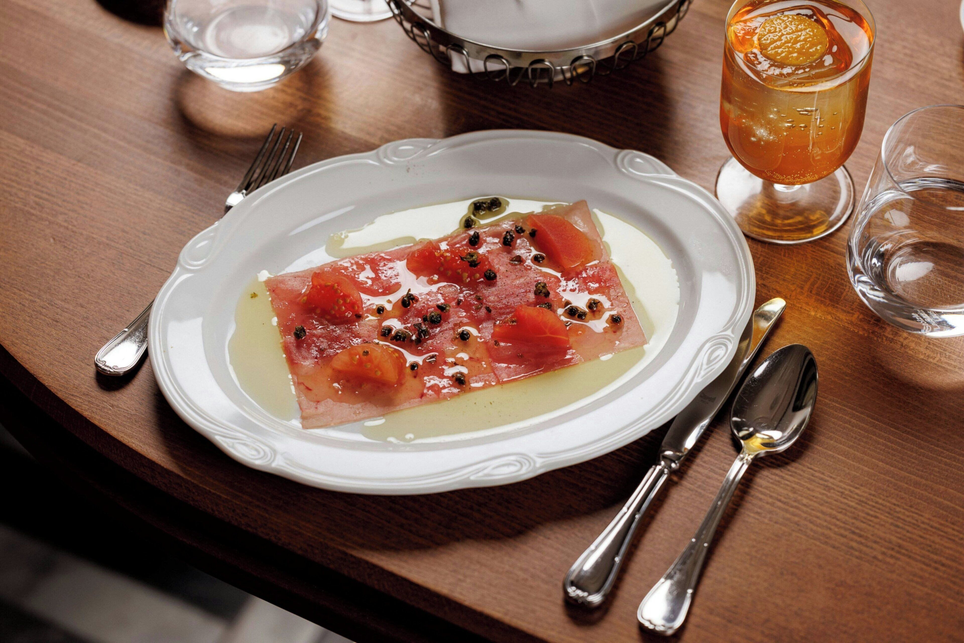 A plate of food on a wooden table with a glass of drink and cutlery.