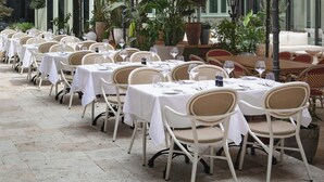 Ein Innenhof mit Tischen und Stühlen, ein Gebäude mit Rundbogenfenstern und Blumentöpfen.