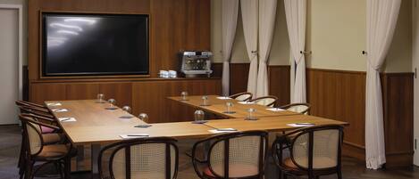 Un salón de conferencias con una larga mesa, sillas, una pantalla de proyector y una máquina de café.